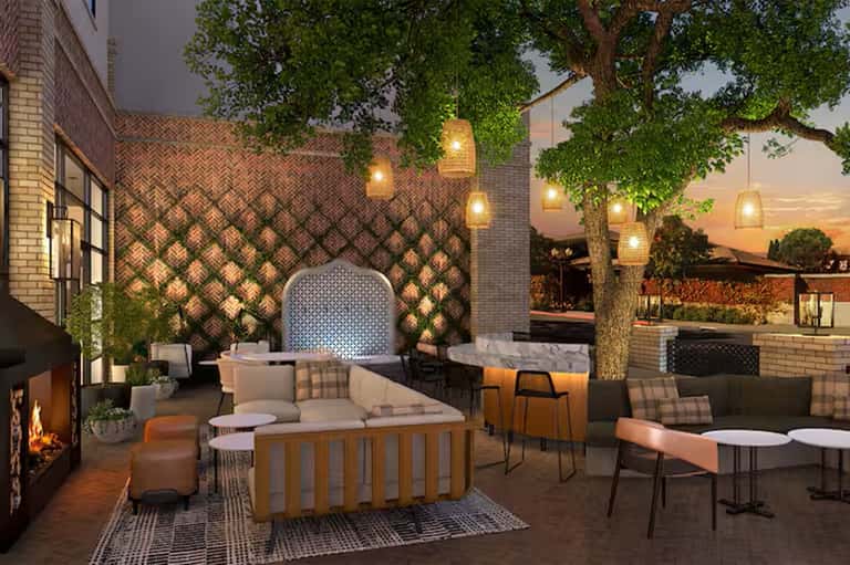 Evening patio with herringbone brick wall, fire pit, hanging lights, loungers, and dining area