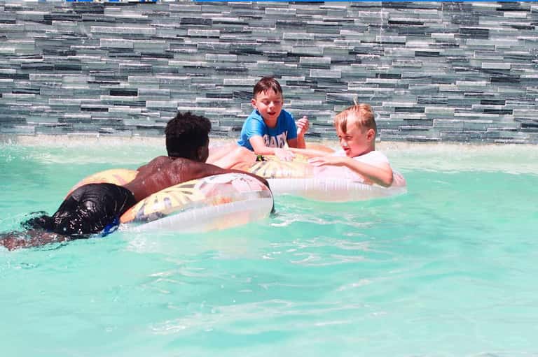 Children and adults floating on inflatable rings in a bright turquoise pool