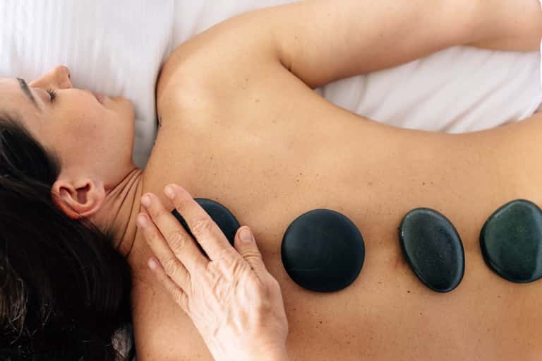Spa massage treatment with heated black stones applied to client's back