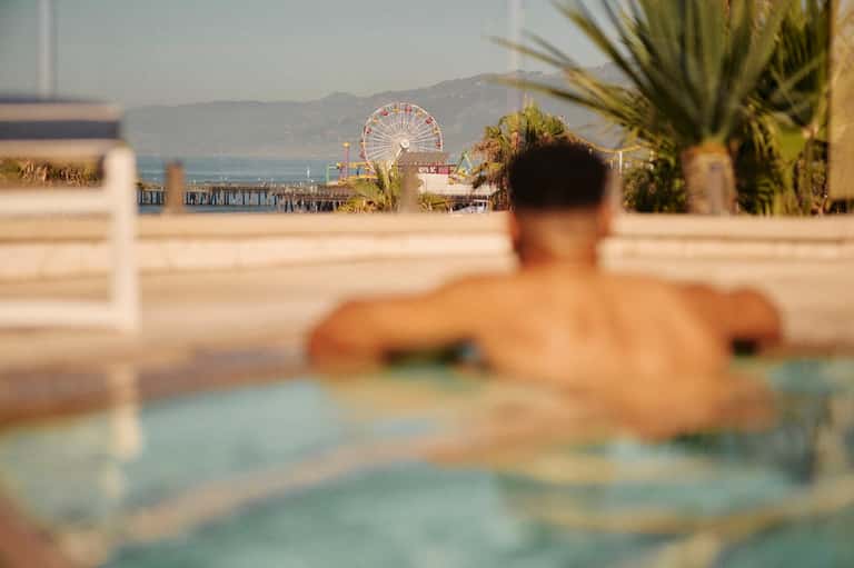 Man swimming in pool with blurred Ferris wheel and pier visible in the background