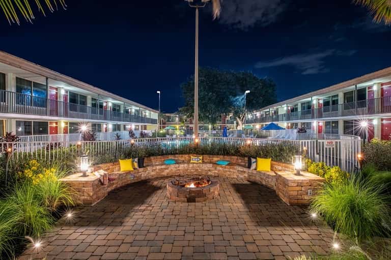 Nighttime resort courtyard with circular stone fire pit, seating, accent lighting, and motel-style building