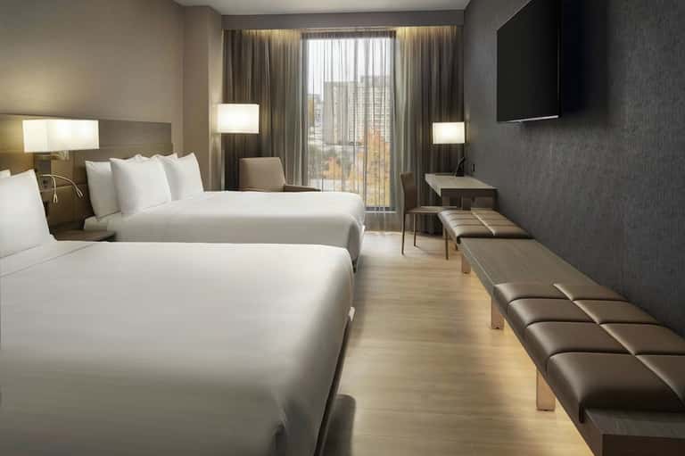 Modern hotel guest room with two queen beds, balcony access, and contemporary furnishings