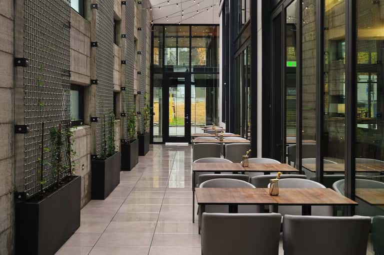 Contemporary outdoor dining terrace with wooden tables, seating, and large windows