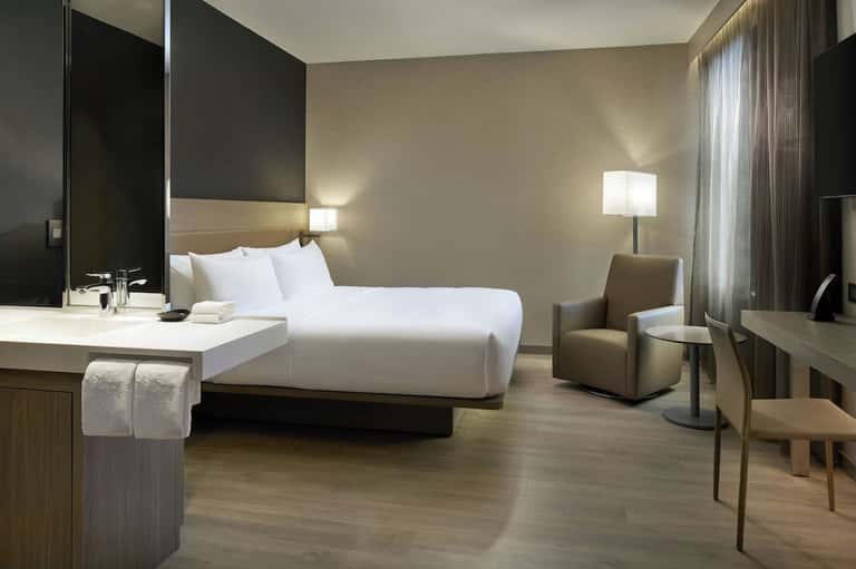 Contemporary hotel room with king bed, white linens, modern desk, and minimalist neutral decor