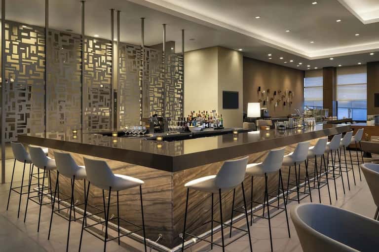 Modern hotel bar with dark countertop, geometric metallic screens, and panoramic waterfront views through windows