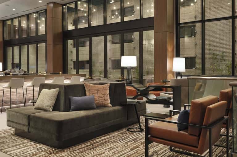 Contemporary hotel lounge with dark sofa, leather chairs, floor lamps, and floor-to-ceiling windows