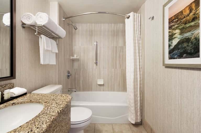 Clean bathroom with double vanity, granite countertop, tiled shower, and natural lighting