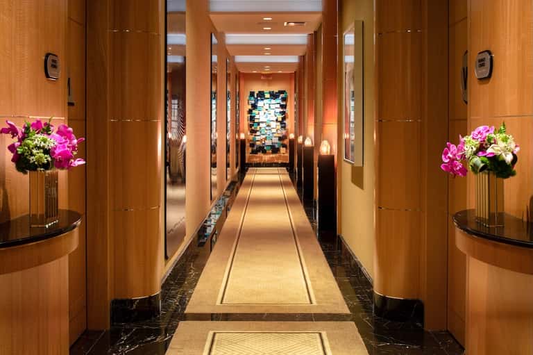 Elegant hotel corridor with warm wood paneling, orchid flowers, mirrored accents, and contemporary lighting