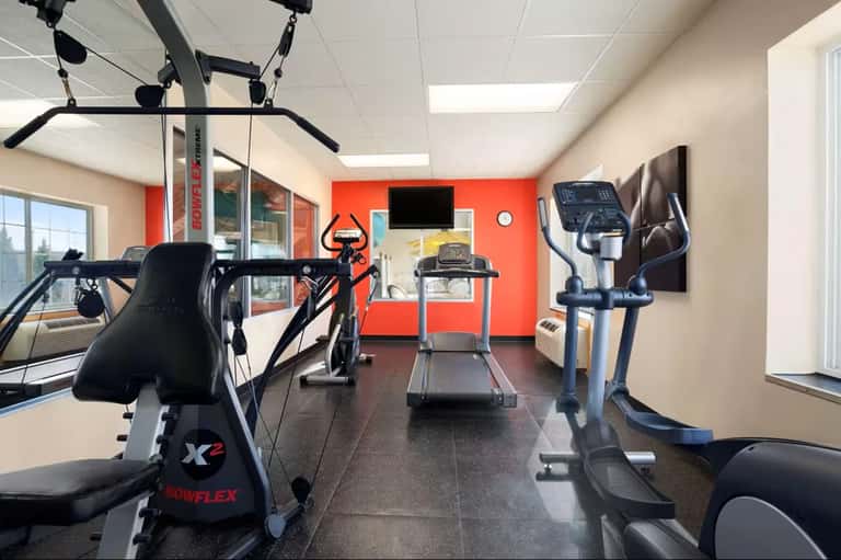 Compact fitness room with stationary bike, treadmill, and exercise equipment against red wall