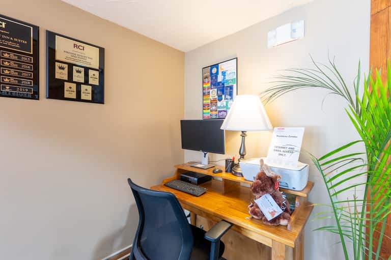 Business center desk with computer, lamp, awards plaques, and green plant decor