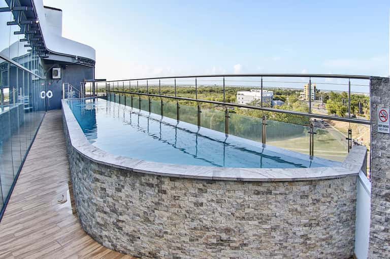 Rooftop curved pool with glass railing, wooden deck, landscape views, and modern architecture