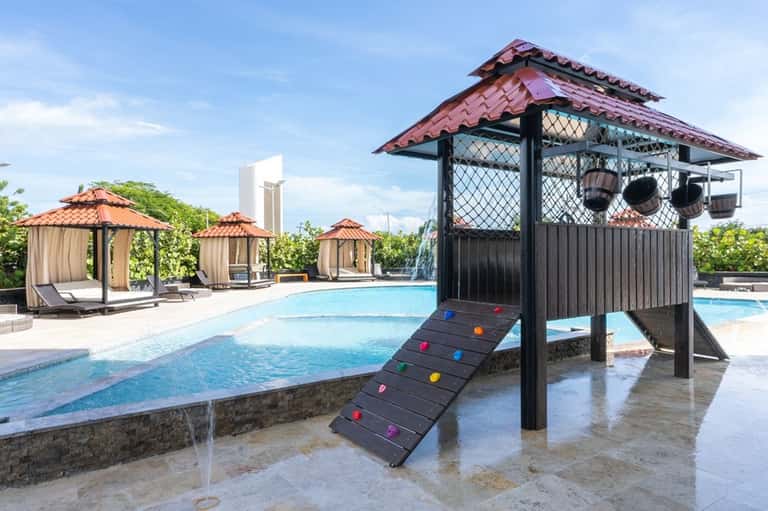 Outdoor pool complex with cabanas, colorful climbing structure, and lounge chairs