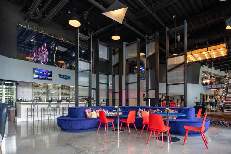 Modern hotel lobby with high ceilings, blue curved seating, red accent chairs, and contemporary bar area