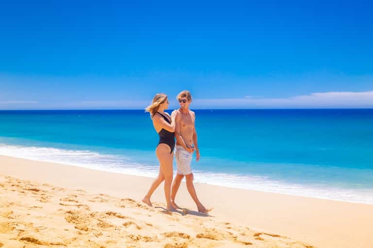 Couple standing together on a pristine sandy beach with turquoise ocean water and clear sky