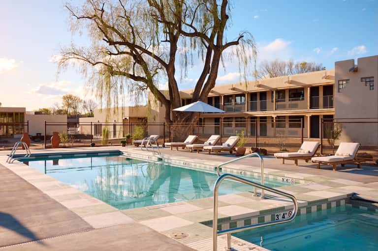 Resort pool courtyard with lounge chairs, weeping willow tree, southwestern-style buildings, and spa facility