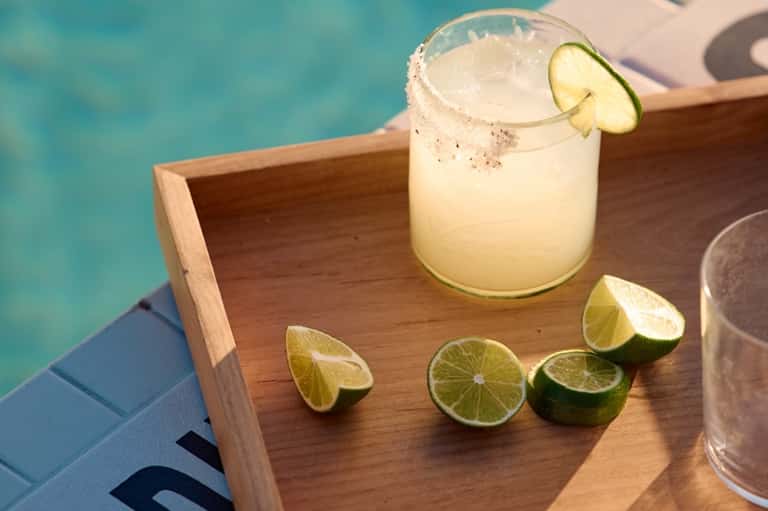 Margarita cocktail with lime garnish on wooden tray by turquoise pool