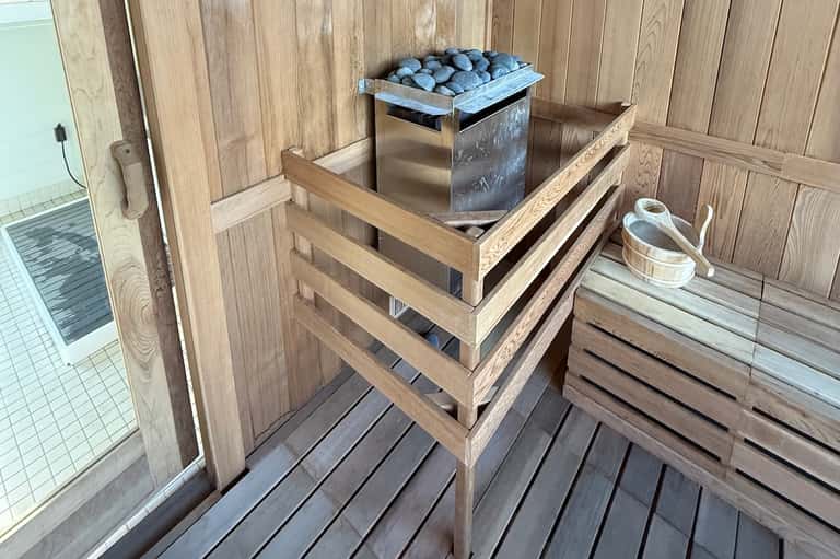 Wooden sauna interior with blue bucket stove, wooden benches, and access to bathroom area