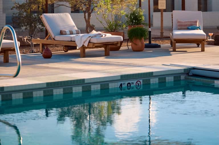 Poolside lounge area with wooden sun loungers, cushions, and small pool with depth markers