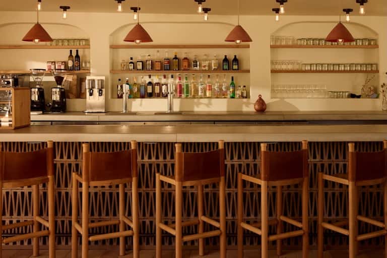 Upscale bar with wooden chairs, copper pendant lights, and shelves stocked with spirits and glassware