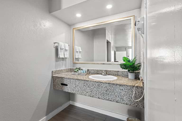 Clean bathroom vanity with granite countertop, illuminated mirror, and white towels