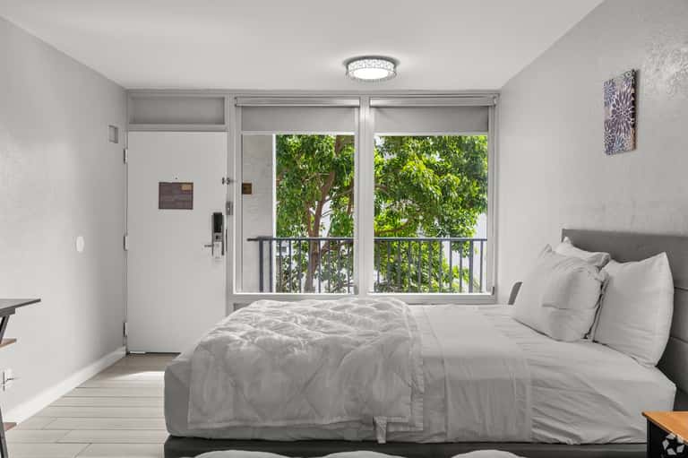 Bright hotel bedroom with modern furnishings and sliding glass door overlooking trees and balcony