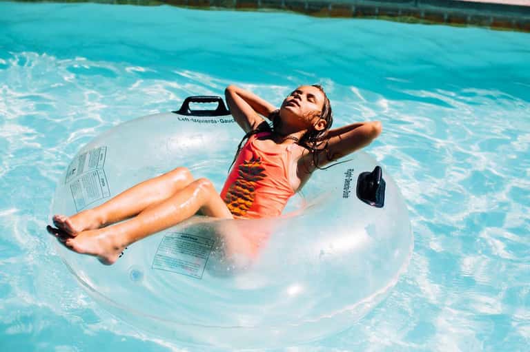Child floating on a clear inflatable ring in a bright turquoise swimming pool