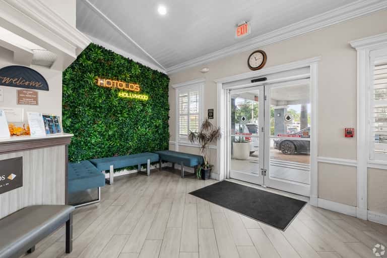 Hotel lobby entrance with green living wall, neon signage, blue seating, and reception desk
