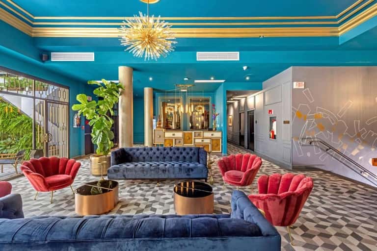 Luxury hotel lobby with turquoise walls, gold chandelier, and colorful velvet seating