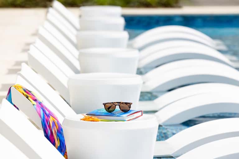 White poolside loungers with colorful scarf and sunglasses beside turquoise swimming pool