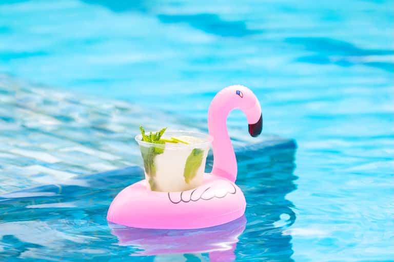 Pink flamingo pool float holding a cocktail in bright blue resort swimming pool