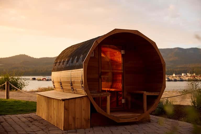 Wooden barrel sauna with glass door overlooking mountain lake and forest landscape