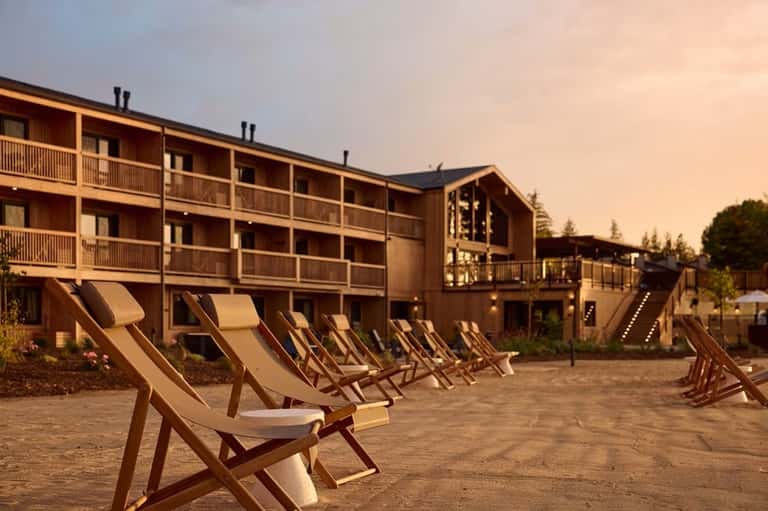 Rustic lodge exterior at dusk with wooden architecture and lounge chairs in courtyard