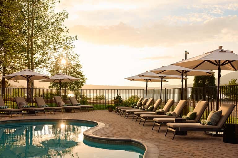 Resort pool at dusk with curved edge, lounge chairs, umbrellas, railing, and manicured lawn