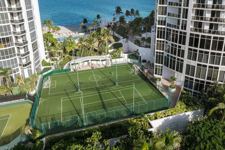Rooftop sports court with soccer field, ocean view, palm trees, and high-rise residential buildings