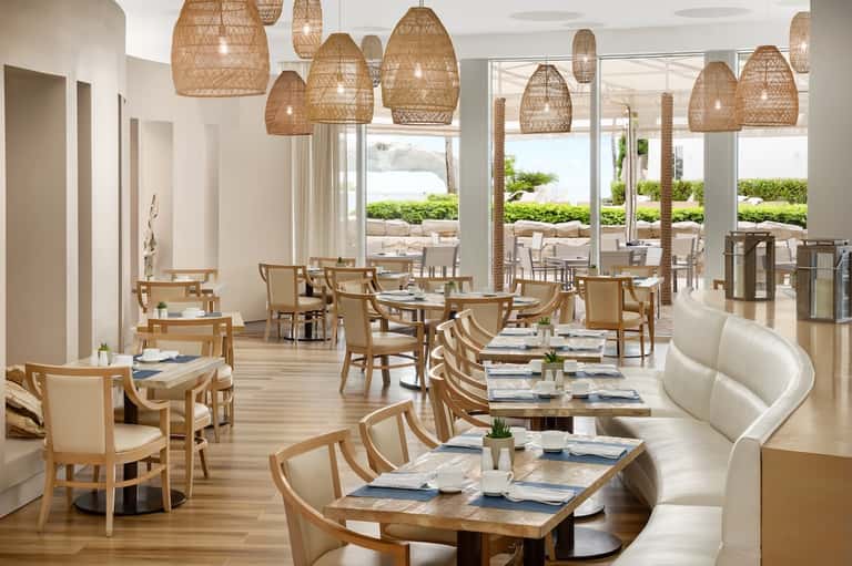 Coastal restaurant with woven pendant lights, natural wood seating, and oceanview terraces