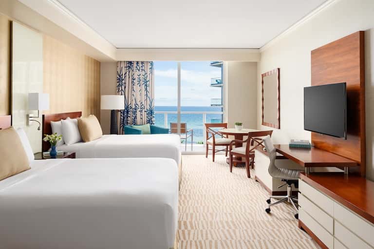 Hotel room with two queen beds, ocean view balcony, and modern furnishings