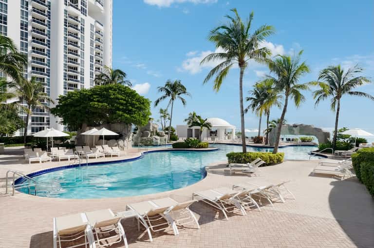 Resort pool deck with lounge chairs, palm trees, and high-rise tower