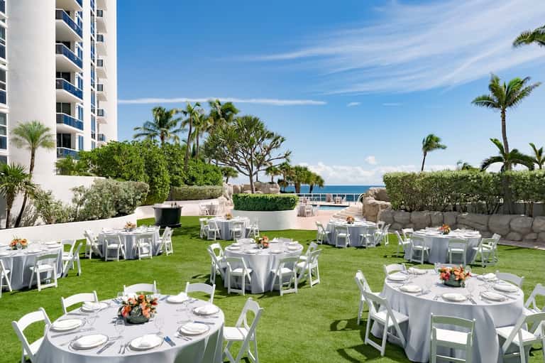 Beachfront wedding reception setup with white tables, chairs, and ocean views on manicured lawn