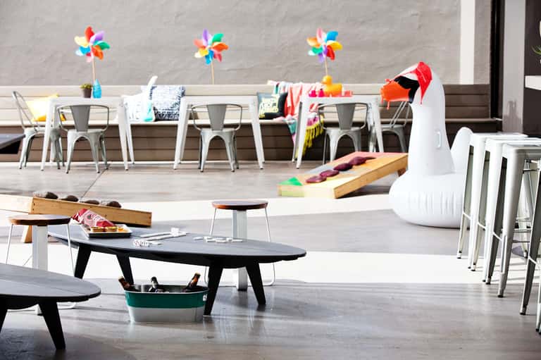 Colorful recreational area with white tables, chairs, pinwheels, and children's activities on a deck overlooking a beach