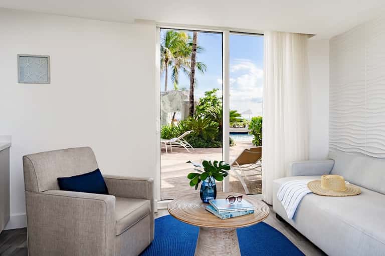Coastal hotel room with balcony view of beach, palm trees, and lounge seating