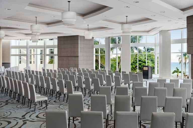 Beachfront conference space with rows of white chairs and ocean view through large windows