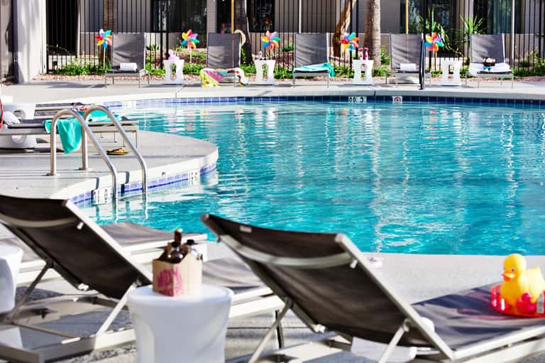 Resort pool with lounge chairs, colorful pinwheel decorations along fence, and modern building backdrop