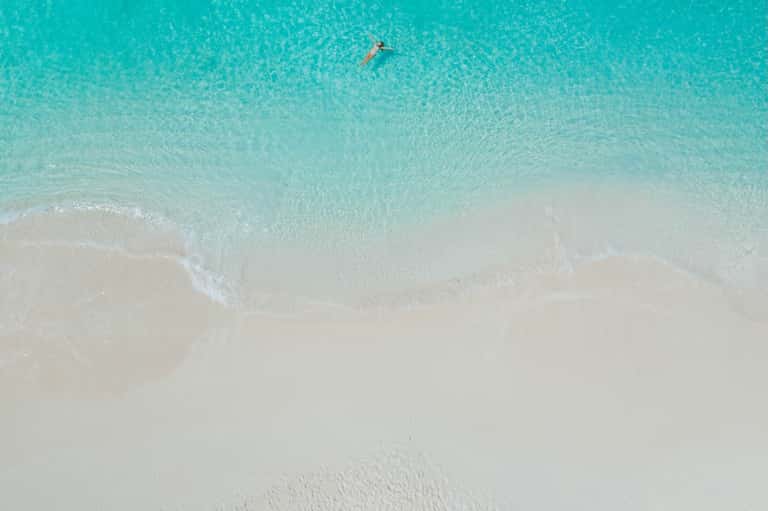 Aerial view of pristine turquoise ocean water with swimmer and white sandy beach