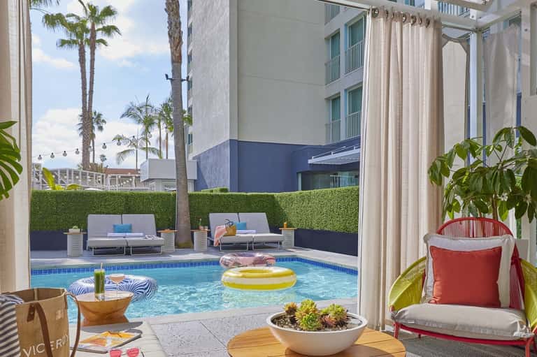 Modern resort pool area with yellow inflatable toy, lounge seating, palm trees, and high-rise buildings