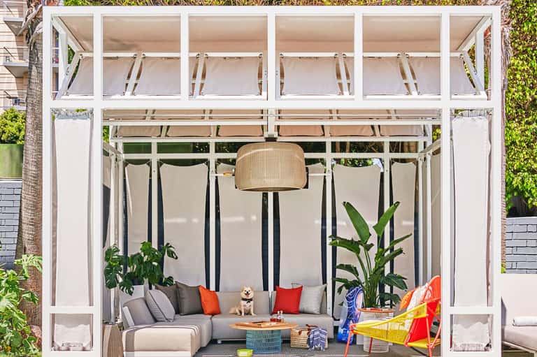 Modern outdoor lounge with white pergola, gray seating, plants, and decorative elements