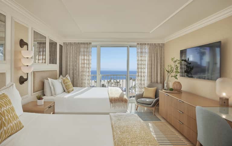 Luxurious oceanview hotel room with two queen beds, balcony, beige decor, and panoramic sea views