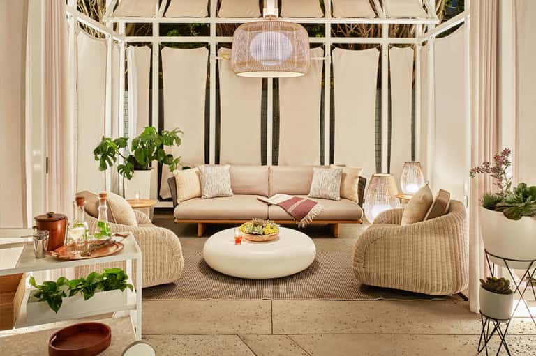 Covered outdoor lounge with wicker furniture, beige sofa, round coffee table, and hanging pendant lamp