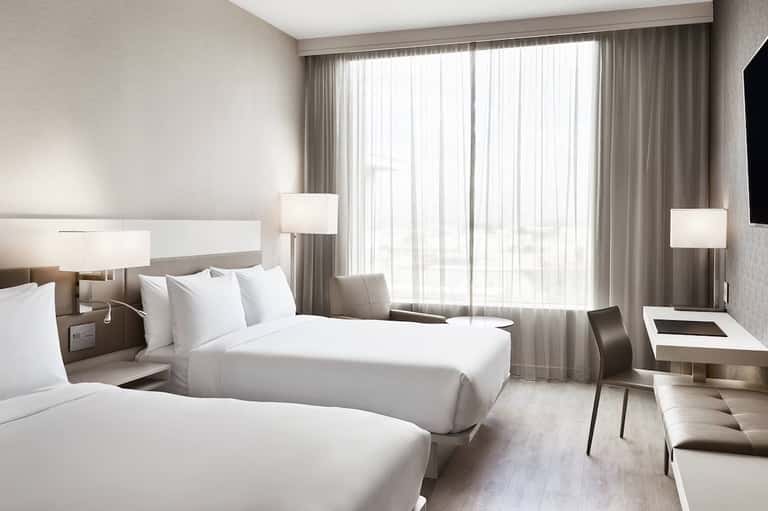 Hotel bedroom with two queen beds, floor-to-ceiling curtains, modern lighting, and contemporary furnishings