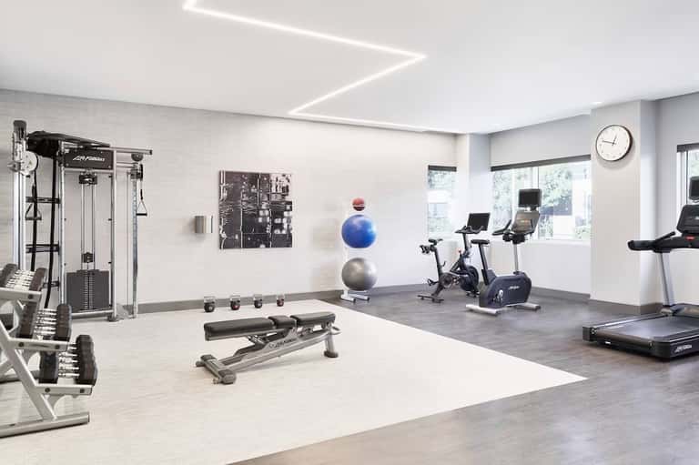 Modern fitness center with white brick walls, exercise equipment, bikes, and large windows with natural lighting.