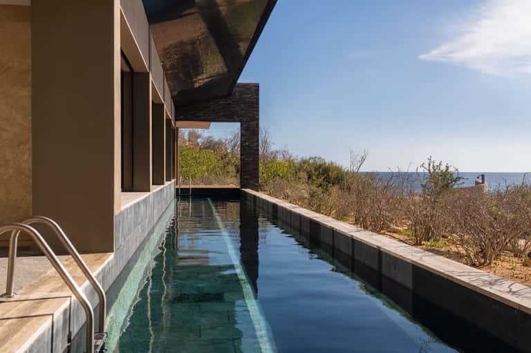 Narrow infinity pool on modern deck overlooking ocean and coastal vegetation